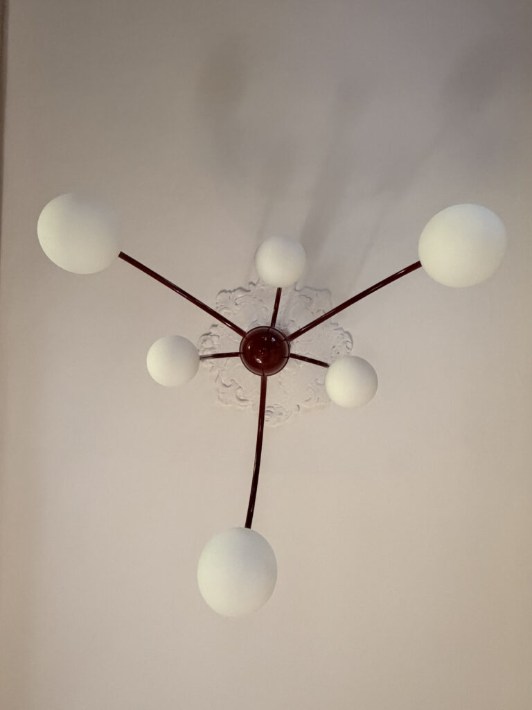 Lampadario design moderno a bracci rossi e globi bianchi installato su rosone in gesso d'epoca restaurato