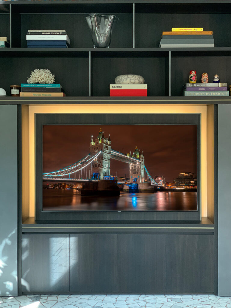 Mobile TV realizzato su misura in legno scuro con nicchia retroilluminata a LED e ripiani per oggetti d'arte e libri di design.