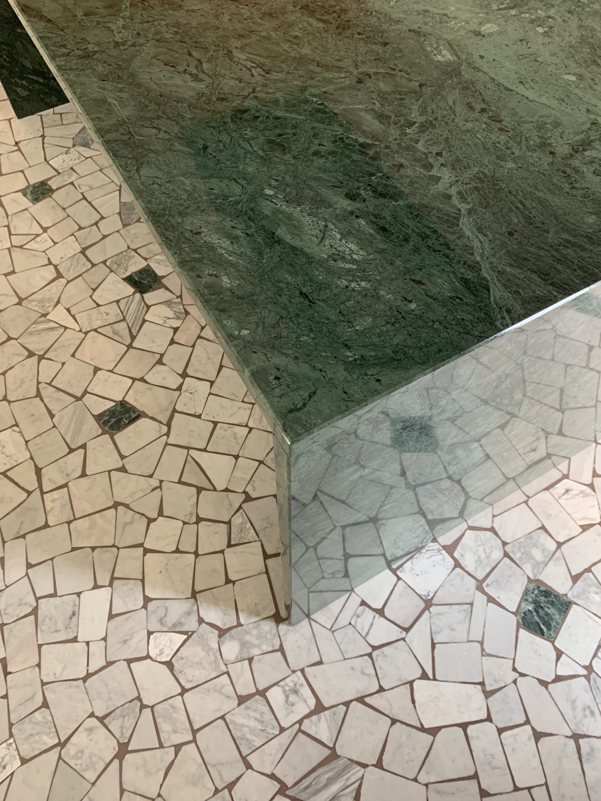 Angolo di un tavolo monolitico in marmo verde Alpi realizzato su misura, in contrasto cromatico con il pavimento originale in palladiana restaurata